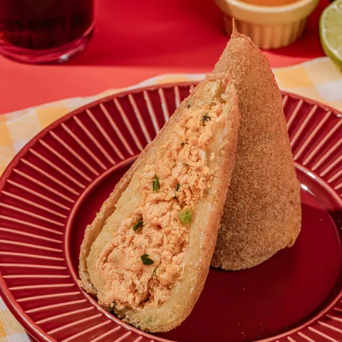 Coxinha de Batata de Frango da Sauté Salgados, cortada ao meio mostrando o recheio de frango desfiado, em um prato vermelho